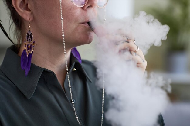 Primer plano de una joven fumadora liberando una nube de vapor espeso blanco