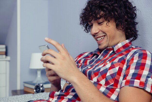 Foto primer plano de un joven guapo mirando smartphone y riendo. concepto de tiempo libre en casa.