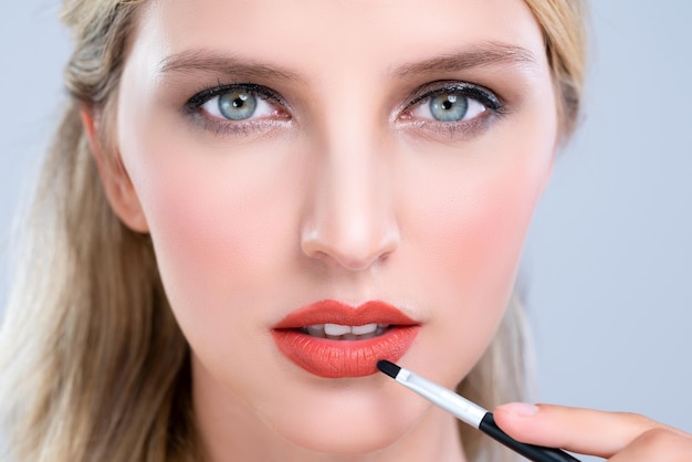 En primer plano una joven hermosa poniendo un lápiz labial rojo brillante de moda seductor