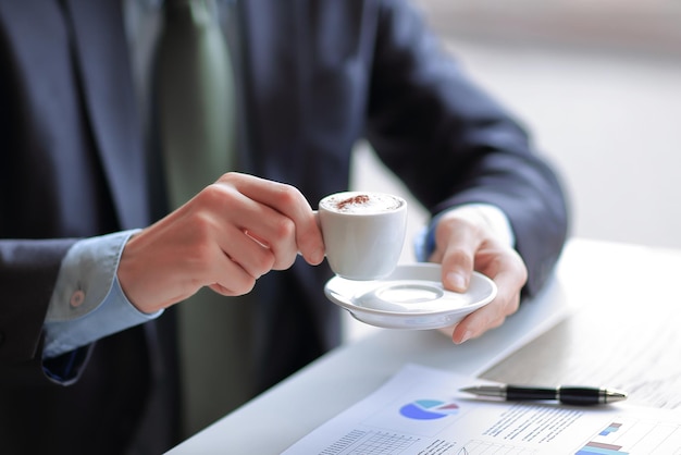 El primer plano de un joven hombre de negocios con una taza de café en la mano revisa algunos gráficos