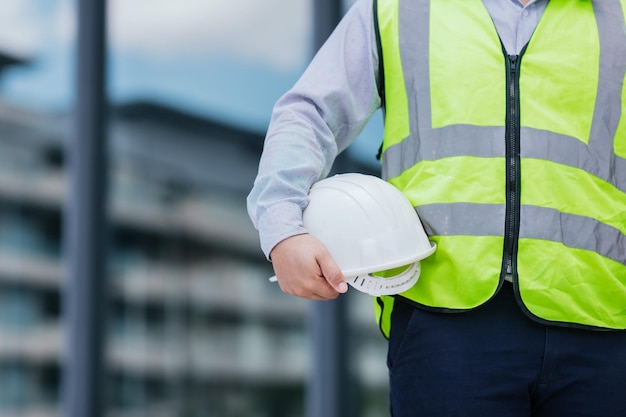 Primer plano de un joven ingeniero con chaleco de seguridad y casco de sujeción en el fondo del sitio de construcción Concepto de trabajador de la construcción de ingeniería