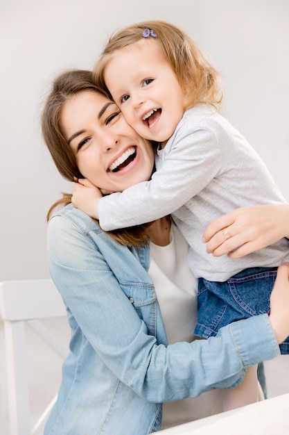 Primer plano de una joven madre morena poniendo y sosteniendo a una niña Atractiva mujer sonriendo