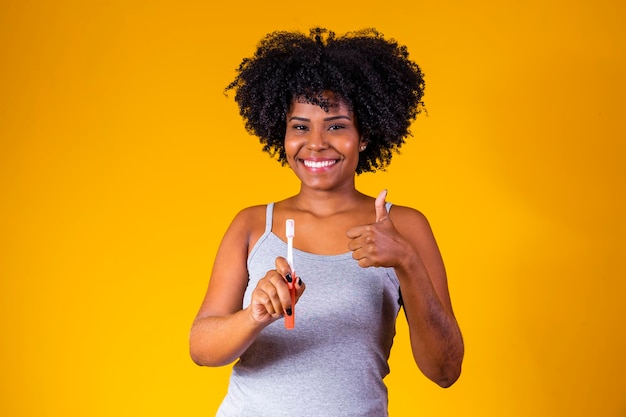 Primer plano de una joven mujer afro sosteniendo un cepillo de dientes sobre fondo amarillo salud bucal