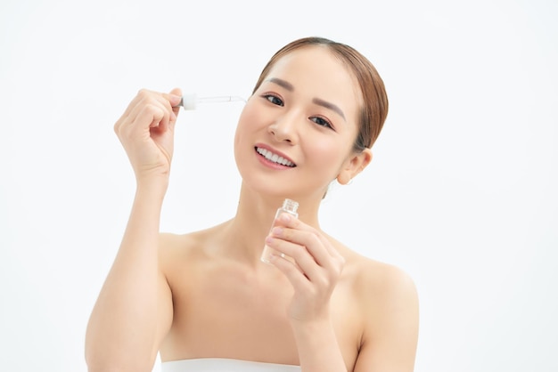 Primer plano joven mujer asiática aplicando suero en su cara aislado fondo blanco.