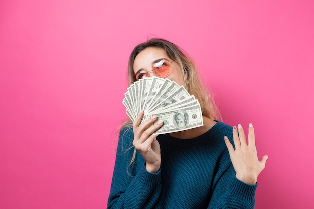 Foto primer plano de una joven mujer hermosa en un suéter azul en vasos con dinero de dólares americanos