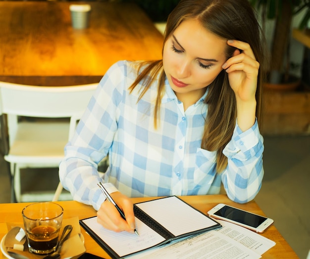 Primer plano de una joven mujer de negocios hermosa escribiendo en un cuaderno