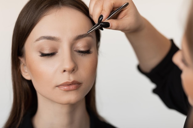 Primer plano de una joven mujer perfecta con el pelo largo y oscuro depilando las cejas por maquillador profesional i