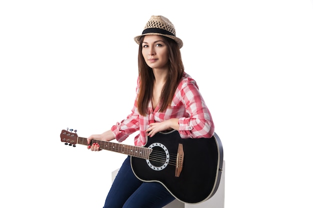 Primer plano de un joven músico con guitarra sentado en un cubo. Fondo blanco.