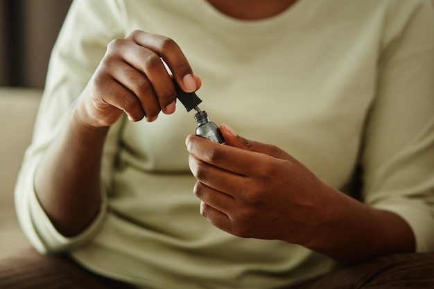 Primer plano de una joven negra sosteniendo una botella de esmalte de uñas plateado mientras hacía manicura en casa