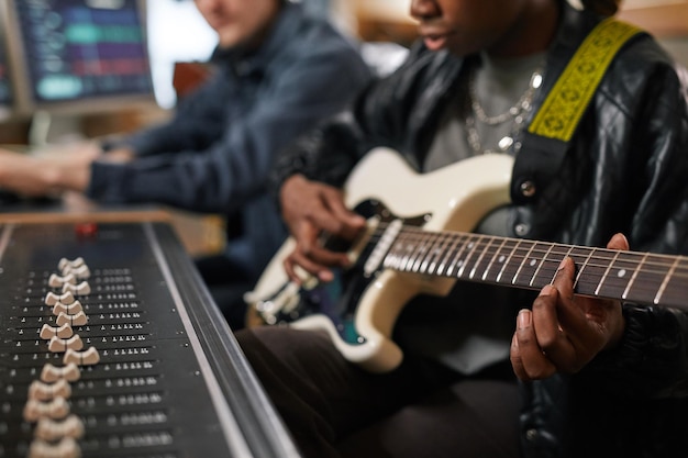 Primer plano de una joven negra tocando la guitarra y cantando mientras compone música en grabación profesional