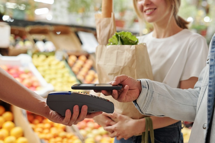 Foto primer plano de la joven pareja pagando productos frescos con el teléfono inteligente en el mercado de alimentos orgánicos