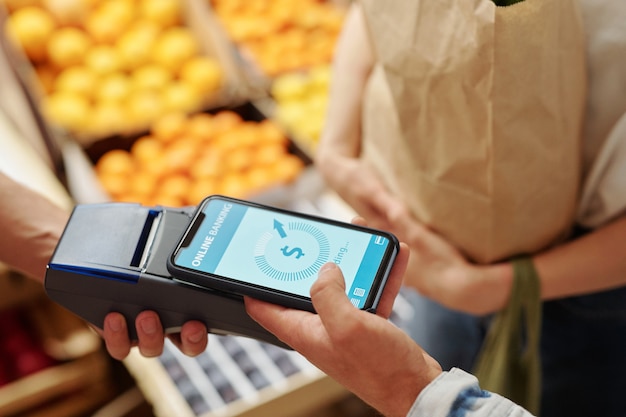 Primer plano de la joven pareja pagando productos frescos con el teléfono inteligente en el mercado de alimentos orgánicos