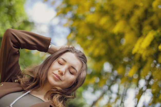 Primer plano de una joven pensativa con los ojos cerrados contra un árbol