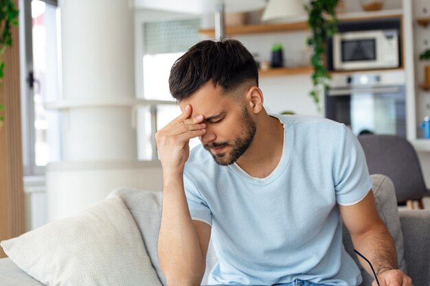 Primer plano de un joven que sufre de dolor de cabeza en casa tocando sus templos copia el espacio borroso de fondo Migraña dolor de cabeza estrés tensión problema resaca concepto