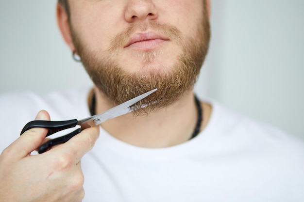 Primer plano de un joven recortándose la barba con tijeras en el interior