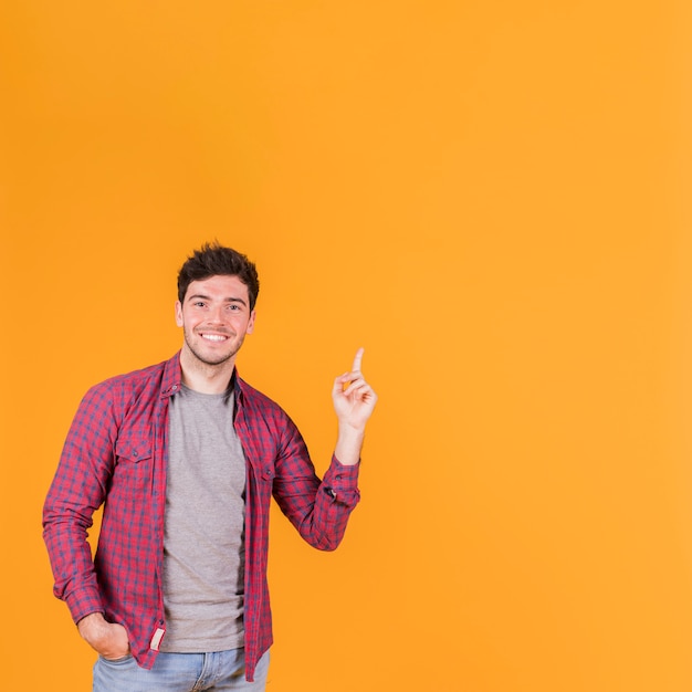 Primer plano de un joven sonriente apuntando su dedo hacia arriba contra un fondo naranja