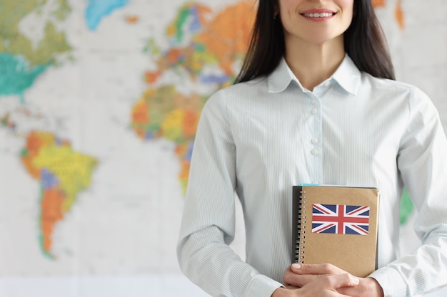 Primer plano de joven sonriente sosteniendo cuadernos con la bandera de Gran Bretaña. Estudiante alegre en camisa. Estudiar el concepto de idioma inglés. Mapa del mundo en el fondo