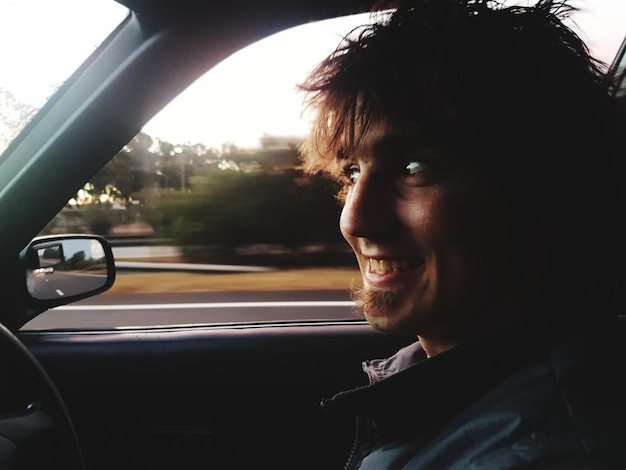 Primer plano de un joven sonriente viajando en coche