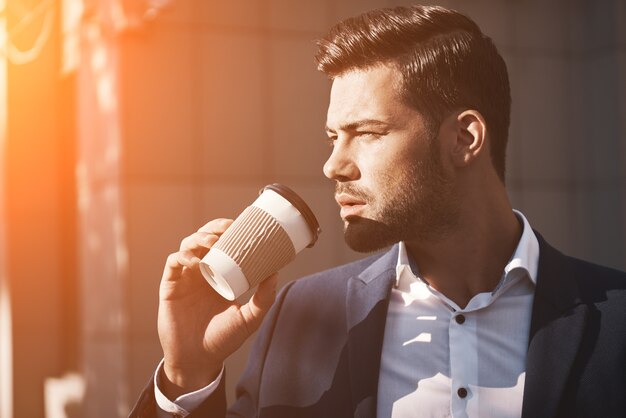 Primer plano de un joven sosteniendo café para llevar temprano en la mañana en el parque soleado