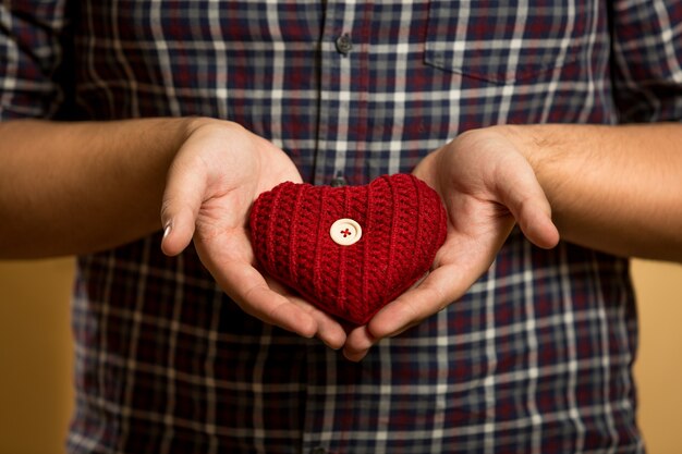 Primer plano de un joven sosteniendo corazón tejido rojo en las manos