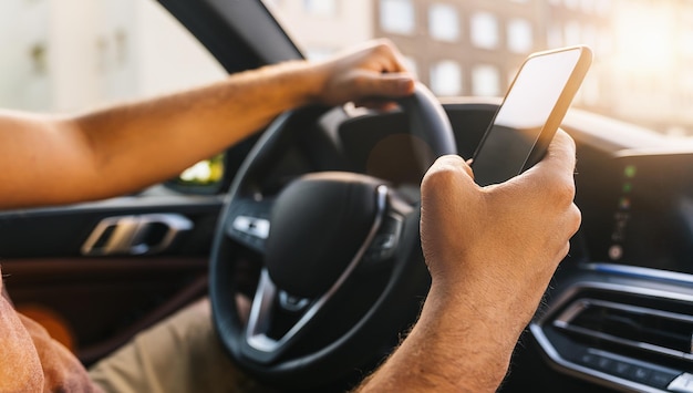 El primer plano de un joven sosteniendo un teléfono móvil en la mano usando el navegador durante la conducción