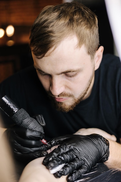 El primer plano de un joven tatuador profesional introduce tinta negra en la piel usando una aguja de un