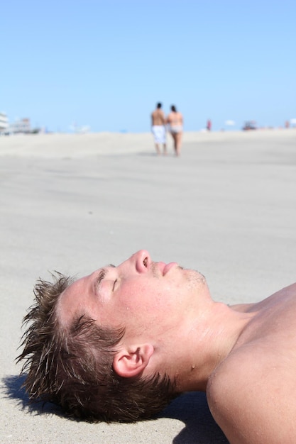 Foto primer plano de un joven tendido en la arena de la playa