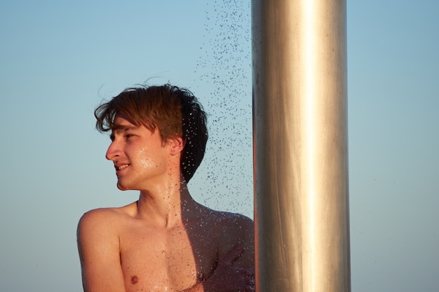 Un primer plano del joven tomando una ducha en la playa.