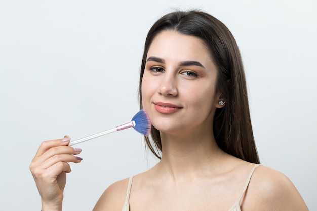 Primer plano de una joven en un top claro sobre un fondo blanco haciendo un maquillaje facial