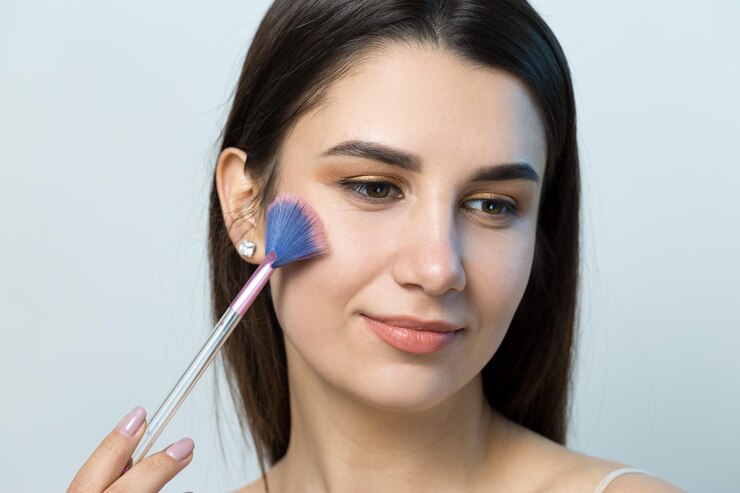 Foto primer plano de una joven en un top claro sobre un fondo blanco haciendo un maquillaje facial