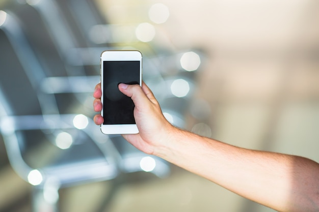 Primer plano de joven usar teléfono inteligente en el aeropuerto interior