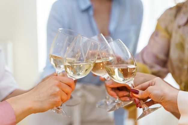 Foto primer plano de jóvenes amigas tintineo de vasos llenos de vino blanco