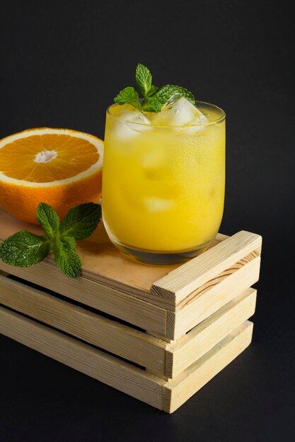 Primer plano de jugo de naranja con hielo en el vaso en la caja de madera sobre fondo negro. Ubicación vertical.