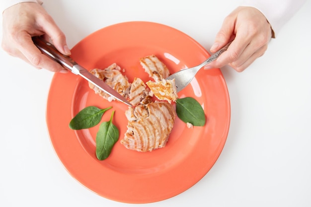 Primer plano de un jugoso y delicioso filete de atún a la parrilla en un plato de coral brillante Comida deliciosa y saludable nutrición adecuada La niña sostiene un tenedor y un cuchillo Vista desde arriba