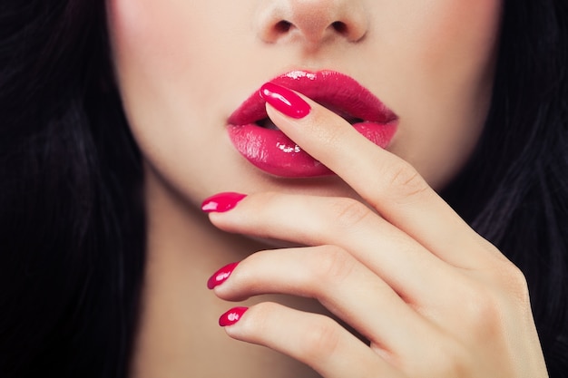 Foto primer plano de labios y uñas femeninas. esmalte de uñas rosa, brillo de labios y cabello castaño. concepto de belleza