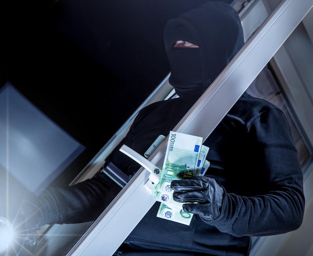 Primer plano de un ladrón con papel moneda de pie al aire libre por la noche