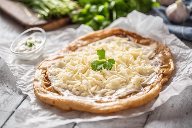 Primer plano de un langos horneado húngaro servido con loevly crema, queso, ajo y cebolla verde fresca.