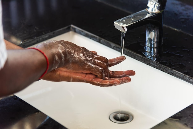 Primer plano lavando las manos del hombre negro frotándose con agua y jabón en los fregaderos para evitar brotes de higiene del coronavirus para detener la propagación del virus, higiene para la limpieza de cuarentena concepto COVID-19