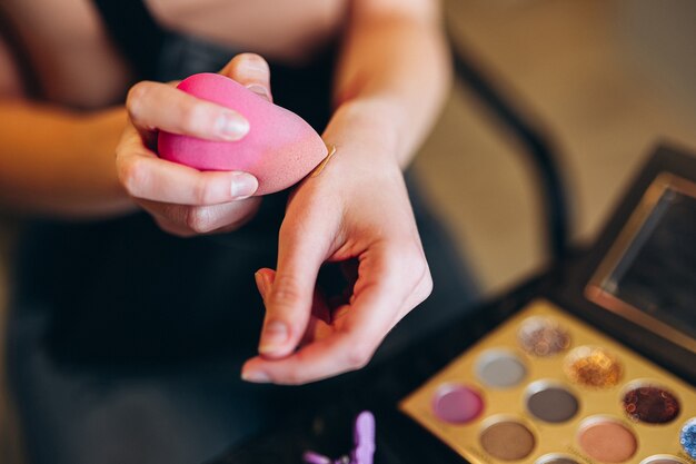 Primer plano de una licuadora de belleza rosa en la mano. La licuadora de belleza recoge el corrector.