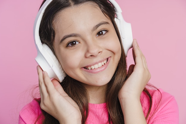 Primer plano, linda, hermosa adolescente escuchando música en auriculares. Chica se divierte sobre un fondo rosa