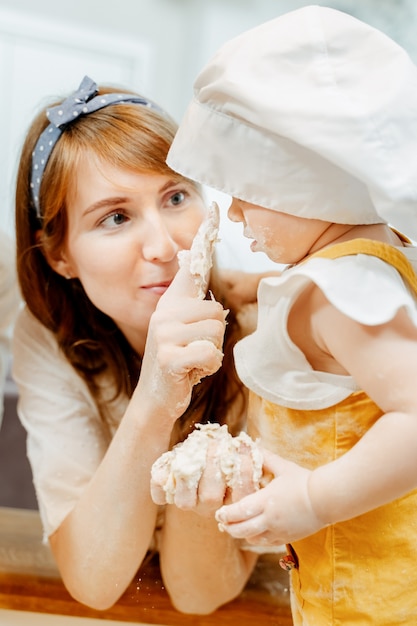 Primer plano de una linda madre cariñosa que muestra a su linda y mugrienta hija cómo hacer masa para buñuelos. Concepto de cocción conjunta con niños en casa