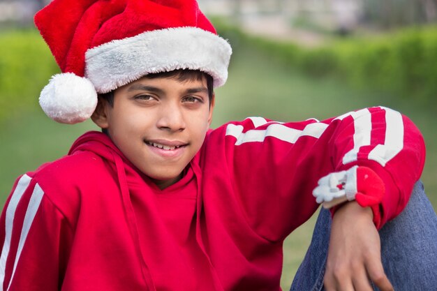 Primer plano de un lindo niño con camiseta roja gorra de Santa sonriendo felizmente y mirando a la cámara