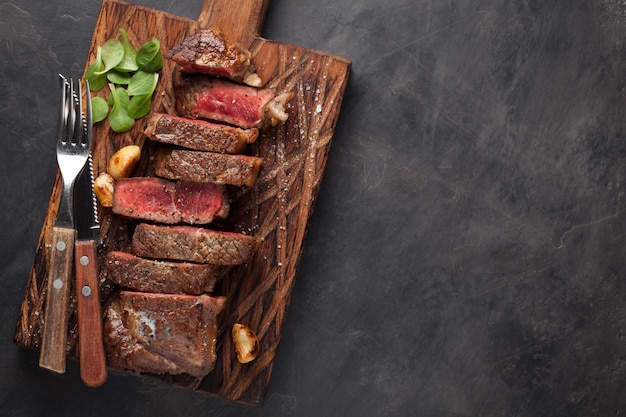Primer plano listo para comer bistec Nueva York razas de carne de Angus negro con hierbas ajo y mantequilla en un tablero de madera El plato terminado para la cena en un fondo de piedra oscura Vista superior con espacio de copia