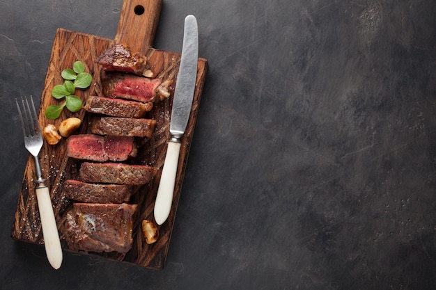 Primer plano listo para comer bistec Nueva York razas de carne de Angus negro con hierbas ajo y mantequilla en un tablero de madera El plato terminado para la cena en un fondo de piedra oscura Vista superior con espacio de copia