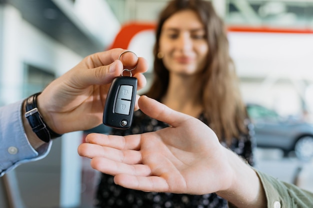 Foto primer plano de las llaves que el gerente del concesionario de automóviles le pasa al hombre en el fondo de una esposa feliz comprando un automóvil familiar