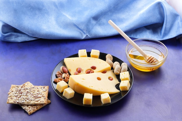 Primer plano de lonchas de queso duro con agujeros grandes y una servilleta azul sobre un fondo azul Lonchas de queso amarillo duro con miel de nueces y panecillos en un plato negro