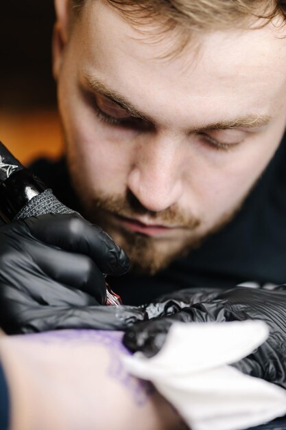 Primer plano del maestro del tatuaje haciendo tatuaje negro con obras maestras de pintura en guantes estériles negros jóvenes