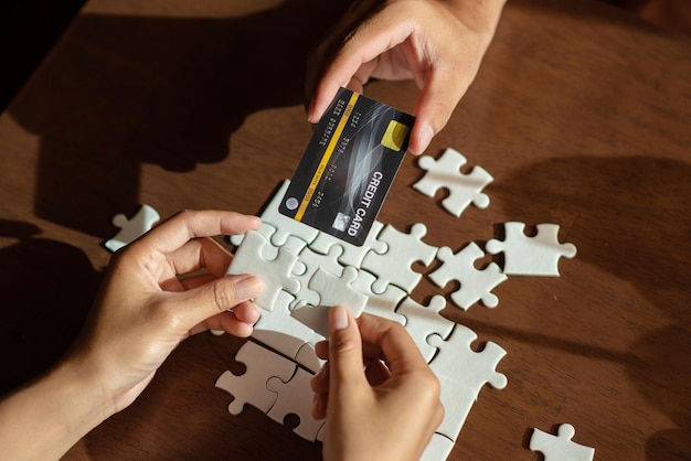 Foto primer plano de la mano arreglando el rompecabezas mientras la persona sostiene la tarjeta de crédito en la mesa