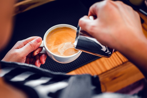 Primer plano de la mano de un barista profesional en una cafetería haciendo verter leche al vapor en una taza