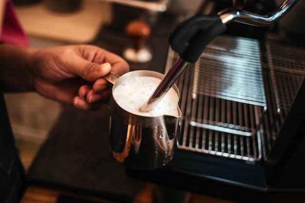 Primer plano de la mano de Barista usando espumador de leche operado por vapor de alta presión para preparar un capuchino